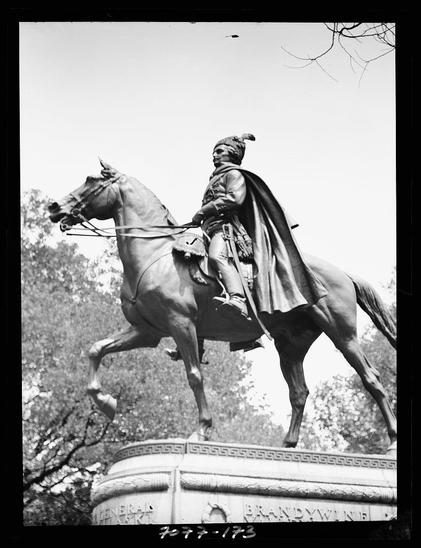 The image is a black and white photograph depicting an equestrian statue of General Brandywine, as indicated by the inscription on its base. The figure represents George Washington in mid-stride atop his horse. He appears to be pointing forward with one hand while holding reins in the other, conveying determination or directive intent. His attire suggests historical accuracy for a military leader from America's colonial period.

The statue is mounted upon an ornate pedestal adorned with relief patterns and inscriptions that are not entirely legible due to resolution constraints but mention "General Brandywine." The background consists of trees which implies the photograph was taken in a park or public square. There appears to be some weathering on both the figure and horse, suggesting age.

This particular statue is part of a series known as equestrian statues found in Washington D.C., dating from 1911-1942 according to provided context. The photographer's name is listed alongside his year active, indicating that Arnold Genthe was involved in capturing this piece of art and history around the early 20th century.

Technical details include a black paper negative with dimensions appropriate for such photographic processes during its time period—indicating an era where nitrate negatives were used commonly. The size mentioned suggests it's on a smaller scale compared to other [...]