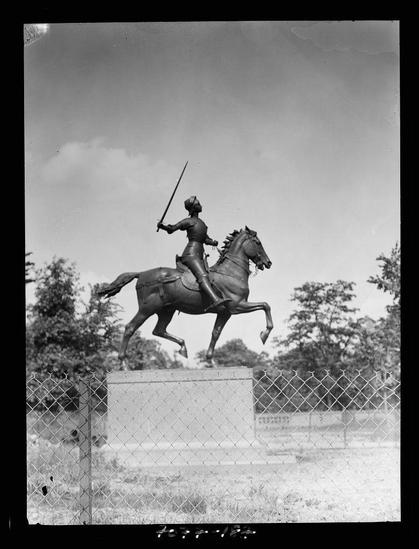 This image depicts a black and white photograph of an equestrian statue, featuring a figure on horseback. The rider is portrayed in mid-motion with one leg raised while holding a sword aloft. They wear what appears to be historical armor or uniform with a hat that has plumes. The horse's head is turned upwards as if looking at the sky, and it also wears bridle gear.

The statue stands on a pedestal within an enclosed area demarcated by a chain-link fence in the foreground. Behind the fenced-off site are trees and what appears to be grassy terrain underfoot. A clear blue sky with few clouds forms the backdrop of this scene.

This photograph is part of a collection or series that may document equestrian statues found within Washington, D.C., during the years between 1911 and 1942 as indicated by the caption provided in Equestrian statues in Washington, D.C. between 1911 and 1942.

The photograph is attributed to Arnold Genthe (1869-1942), a renowned photographer known for his work during that era capturing significant historical moments through photography. The negative on which this image was made suggests it's part of the nitrate film format, common in early photographic practice before the advent of silver gelatin or other more modern films.

The dimensions specified (4 x 5 inches) suggest a large-format photograph, typical for studio work and fine art prints during Gent [...]