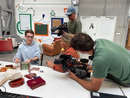 Photo d'une personne qui présente un projet technique réalisé au fablab d'Hyperlien, entourée par des caméramans et une journaliste.