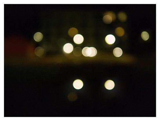 En liggande bild på ett hus i mörkret, men är så ur fokus att ljusbubblor är det enda som syns förutom svaga konturer.