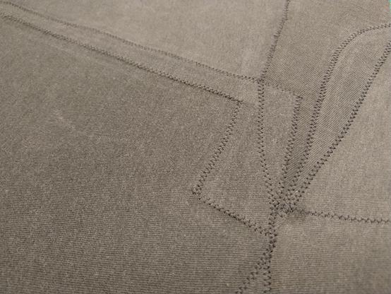 A piece of faded black fabric made from irregular scraps joined together with zigzag machine stitching. It’s not super-obvious from the photo, but the scraps are all faded differently and probably come from different sources.