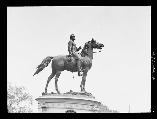 The image is a black and white photograph of an equestrian statue, depicting a man in military attire mounted on horseback. The figure appears to be looking off into the distance with one hand gripping what seems like reins or bridle straps while holding a sword aloft in his other arm.
Below this central figure stands another larger equine form supporting it; both seem to sit atop an ornate pedestal that is adorned with decorative elements such as floral designs and circular motifs. In the background, faint outlines of trees can be seen against what appears to be a clear sky. The statue's composition conveys themes of military valor or historical significance.
Additional context for this image indicates it belongs to the collection at Loener Archives, highlighting Arnold Genthe (1869-1942) as an artist associated with photography during 1911 through 1942 in Washington D.C. The photograph is one of a series related to equestrian statues from that time period within this cityscape.
The physical dimensions mentioned suggest the photo has been preserved on negative material, like nitrate or similar film formats commonly used for photographic negatives during Genthe's active years as an artist and photographer.