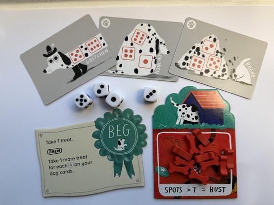 Cards and components from the board game Spots designed by Alex Hague, Jon Perry, Justin Vickers with art by John Bond. There are three dog cards each showing 11 spots. There are 4 dice showing a total of 11 spots and there are 11 bones on the player board which shows a dog sticking its head in a dog house. A trick tile is also shown which would give the player the ability to take 1 more treat than usual. All the dogs are good dogs.