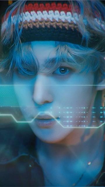 Ateez Yunho dans le MV de Crazy Form. 
Portrait tres serré sur son visage et le haut de son buste. A les cheveux gris clairs qui lui tombent sur les yeux et porte un bandeau en grosses mailles et à rayures noires, rouges, jaunes et marrons sur le front. 
On peut voir en transparence devant lui une sorte d’interface numérique inspiration de l’imagerie du code et de la programmation à la fois rétro et futuriste (pour faire simple : représentation d’une interface qui ne veut rien dire mais qui fait mystique, clairement inspirée de Matrix sauf que la vibe est bleue plutôt que verte).