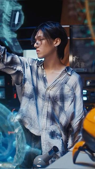 Ateez Wooyoung dans le MV de Crazy Form. 
De profil, chemise à carreaux gris clairs et foncés, à moitié rentrée dans son pantalon. A le bras droit en l’air et il regarde dans cette même direction. 
Cheveux noirs, paire de lunettes métallisées, boucle d’oreille. 

On peut voir en transparence devant et autour de lui une sorte d’interface numérique inspiration de l’imagerie du code et de la programmation à la fois rétro et futuriste.
Or celle-ci fait un poil plus de sens puisqu’elle présente des images de certains éléments importants du lore de Ateez comme un très grand gouvernail en premier plan à gauche.