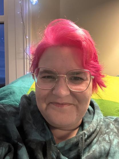 Clair is smiling at the camera, with vibrant pink hair.