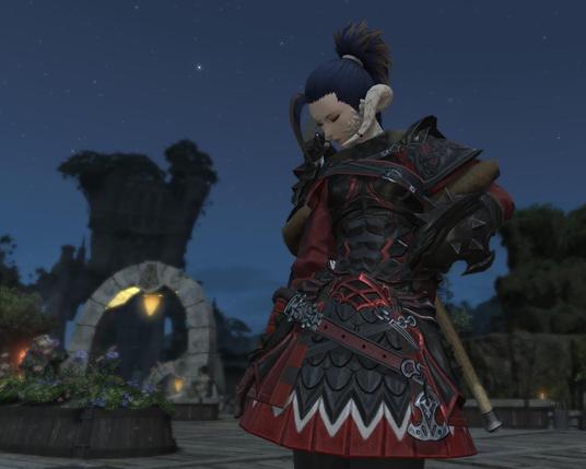 FFXIV screenshot player character female au’ra wearing red and black armor standing in front of a stone arch at night.
