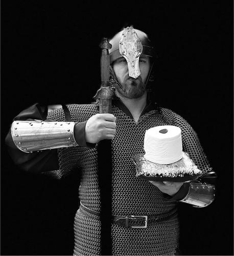 Photo of a man in chainmail, plate bracers, and a helm holding a sheathed sword and a platter with a roll of toilet paper on top.