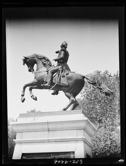 The image displays a black and white photograph of an equestrian statue featuring a figure in historical military attire, mounted on horseback. The rider is depicted with raised legs as if leaping or galloping forward. This bronze sculpture is perched atop a rectangular stone pedestal. The background includes trees and the sky, suggesting that this monument stands outdoors within a public space likely to be of significance for its commemorative value.

The statue captures motion through its dynamic pose, emphasizing strength and vigor. The rider's posture indicates control over the horse while conveying determination or leadership qualities typically associated with military figures in history. There is no clear indication as to who specifically this figure represents, which may suggest that it commemorates a general historical event rather than an individual.

The image itself has visible text at its base indicating "7018-2/9", possibly serving as an identification number or cataloging information for the photograph within a collection. Additionally, there is reference to Equestrian statues in Washington, D.C., which spans from 1911 to 1942, suggesting that this statue could be part of a series documenting equestrian monuments erected during that era.

Furthermore, the image credits "Genthe, Arnold" as likely the photographer or an associated contributor. The mention of  [...]