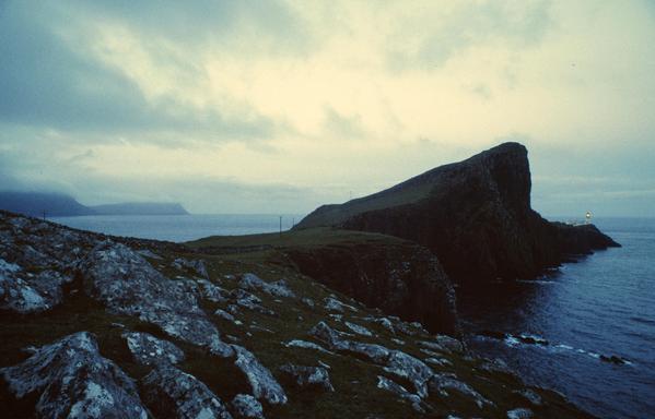 The huge triangular rock The Stallion lies before the tiny looking lighthouse at the coast of Neist Point