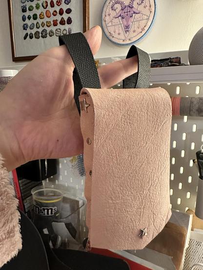 L’étui rose est suspendu à deux boucles de cuir noir qui s’accrocheront à ma ceinture arc en ciel. Sur le mur du fond, deux jolies broderies maison.