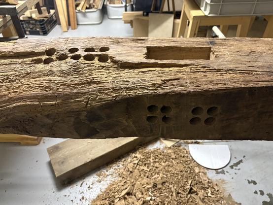 An old barn post with holes bored into it for chopping mortises.