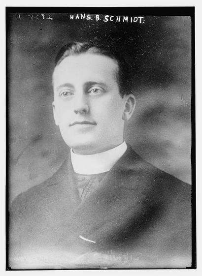 The image is a black-and-white portrait of a man. The man appears to be dressed in formal attire, including a suit with a white collared shirt and a tie. His hair is neatly combed back, and his expression is serious, with a slight upward curve of his mouth, giving a hint of a smile. The photograph has a vintage appearance, suggesting it is from an earlier time period, possibly the early 20th century. The background is plain and dark, which helps to focus attention on the subject. At the top of the image, there is text that reads "HANS B. B. SCHMIDT," which appears to be the name of the individual. The style and quality of the image, along with the text, suggest it might be a historical photograph.