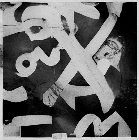The image is a black‑and‑white abstract composition dominated by large, bold, curving shapes that resemble fragments of numbers or letters scattered across the frame. Several thick, pale forms sweep diagonally from corner to corner over a darker background, creating a strong contrast and a sense of overlapping layers.  

Near the left side, one prominent shape looks like a rotated numeral “2” with a circular opening, lying at an angle so that it almost appears to be falling or twisting. Around it are other partial forms that could be parts of “3,” “5,” or similar glyphs, but they are cropped and tilted so extremely that they become almost unrecognizable and purely graphic. Toward the right edge, a lighter patch suggests a torn or worn surface, with rough texture and irregular edges that contrast with the smoother, printed‑looking curves elsewhere.  

Cracks, scratches, and small tears run through many of the pale shapes, giving the impression of weathered paper or peeling posters that have been layered and then partially destroyed. The background is mostly dark and uneven, with subtle tonal variations that hint at shadows or underlying material beneath the top layer.