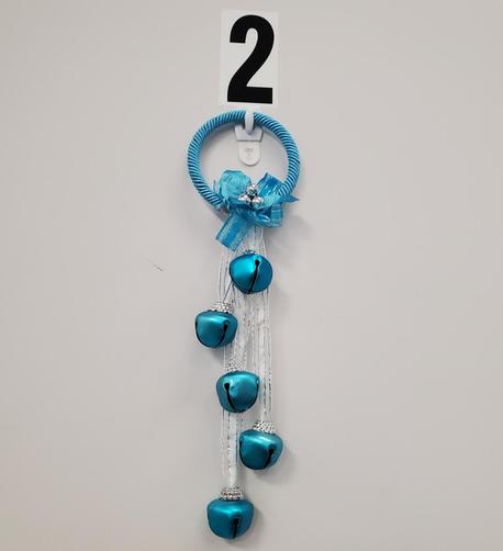 A teal Christmas bell decoration with four bells, a teal bow and rope, silver accents and hanging from the wall below a black "2".