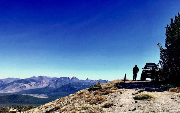 Deadmann Pass, Eastern Sierra. A man stands next to a Jeep XJ, surveying the view. There are snow capped mountains in the distance.