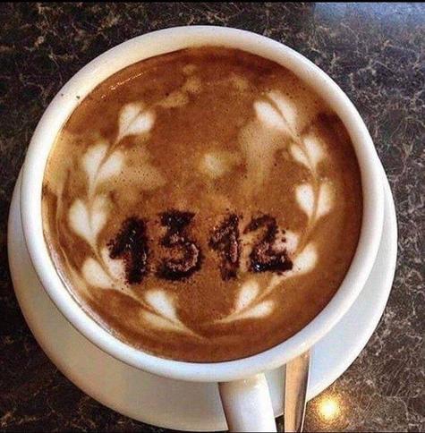 Une tasse café vu de dessus. Dans la mousse brune est écrit 1312 en poudre de chocolat.