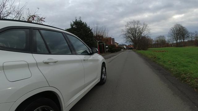 Ein weißes KFZ überholt einen Radfahrenden mit deutlich zu wenig Abstand. Das Bild ist aus der Lenkerperspektive aufgenommen.