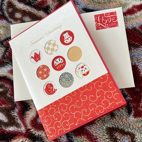The front design of the holiday card is shown atop of the envelope with the red “love” stamp. The card has 9 small round windows with different iconic Japanese images on them, such as a red crane, maneki neko (welcoming cat), a daruma (a round good luck figurine that signify perseverance), a red leaping carp, and so on. The bottom of the card has a red obi with gold squiggles that symbolizes heavenly clouds. It’s a beautiful card.