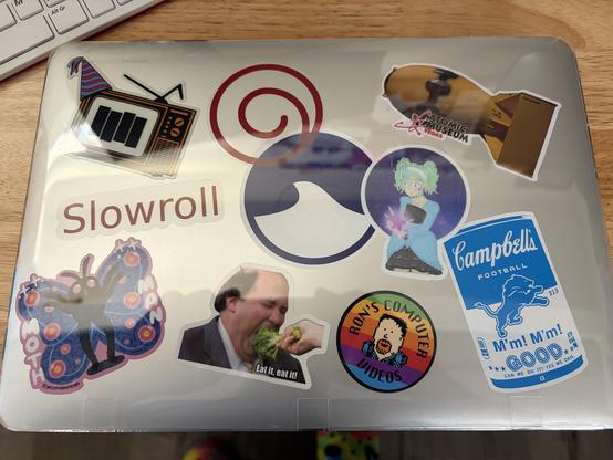 Macbook with various stickers on the top with a clear case.