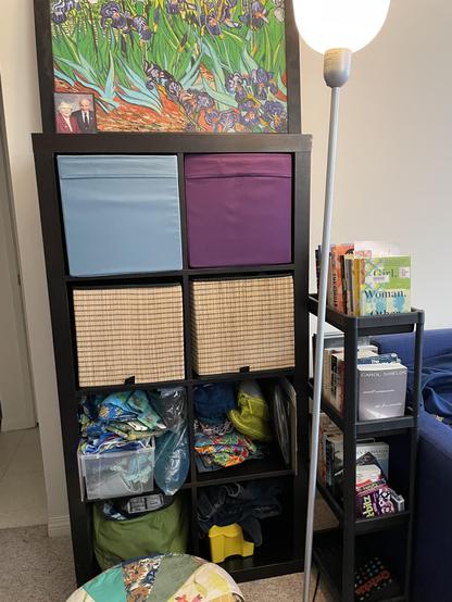 An IKEA Kallax organizer is filled with fabrics for future projects. A small shelf set contains books, including library book club books