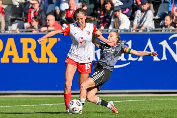 Maj Schneider führt den Ball am Fuß, von der Seite grätscht Elisa Senß rein und hält sie an einem Arm.