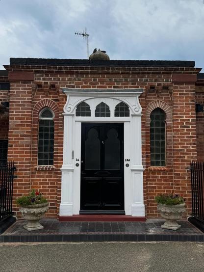 A black door with two window panels set into an ornate white surround, in a red brick wall with tall windows. The number 14 is on one side of the door, and 14A on the other.