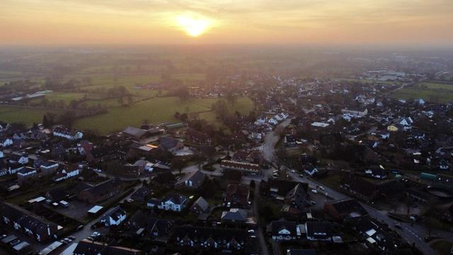 Luftbildaufnahme auf ein Dorf, am Horizont die orange leuchtende Sonne.