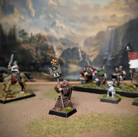 Miniatura de warhammer de un monje orondo con hábiro de monje marrón sosteniendo un tríptico de madera, mirando a cámara.