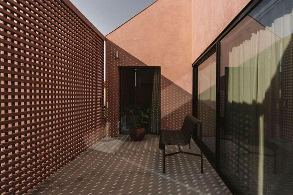 A modern patio with textured walls, a curved bench, and a patterned wooden fence casting playful shadows on the floor.