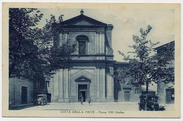 The image depicts a historical postcard featuring the Città della Pieve, specifically highlighting "Piazza VIII Ottobre" in Italy. The architecture is classical with columns and pediment details that suggest it's likely to be a church or an important civic building. There are trees partially obscuring parts of the structure on either side, giving a sense of age and perhaps seasonal change as they have dense foliage. A vintage vehicle can be seen parked by the curb in front of what appears to be another older two-story building with barred windows, typical of urban European architecture.

In the foreground, there are figures that seem small due to perspective; one figure is walking towards or away from a door on the left side and others appear smaller and farther down the street. The postcard has text in Italian at the bottom indicating its location: "CITTÀ DELLA PIEVE - Piazza VIII Ottobre." There's also some visible wear around the edges, suggesting age.

The image is monochromatic with a deep blue tint that gives it an aged look consistent with old photographs or prints. The overall impression is one of historical significance and captures a moment in time within this particular town square over 100 years ago.