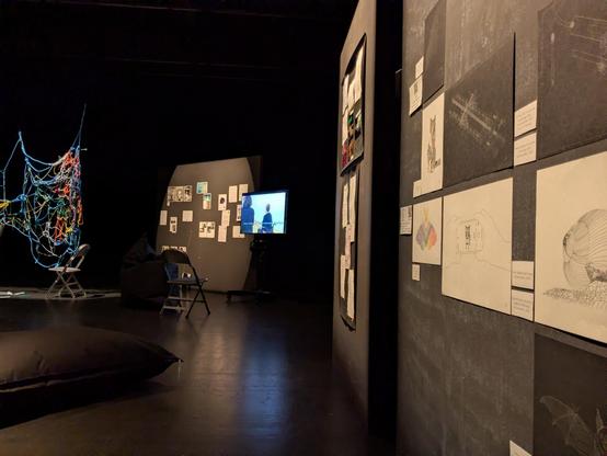 the same wall, with a bit more of the exhibition room visible. in the left corner is a coarsely woven net made out of colorful rope