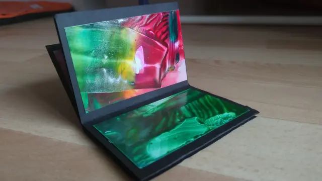 Das gefaltete Papier liegt auf dem Boden, zu sehen sind zwei kleine Karten im ungefähren Format A7. Hauptfarbe grün.