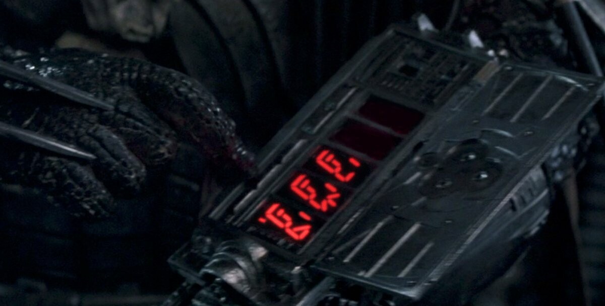 A screenshot from the movie Predator, where the predator appears to be arming its wrist bomb, but instead of digits counting down it's the members of The Police in bright red segmented digit-like illustrations from the album cover of Ghost In The Machine.