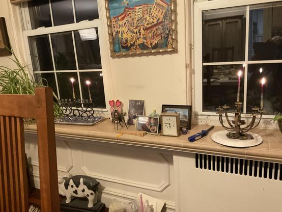 Cluttered windowsill with two windows, a Hanukkah menorah in each one.