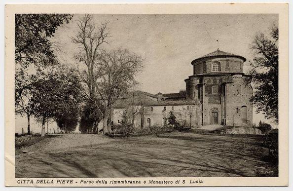 The image displays an old black and white photograph of a historical building, which appears to be a church or monastery. The structure features classical architectural elements such as rounded apses on the sides, arched windows, and stone masonry that suggests age and historical significance. It's set against a backdrop with leafless trees indicating it might have been taken in late autumn or winter, although some greenery is visible too.

The photograph bears text at the bottom which reads "GITTÀ DELLA PIEVE - Parco della rimembranza e Monastero di S Lucia," suggesting that this location is named Pieve and includes a memorial park with St. Lucia's monastery within it in Città della Pieve, likely an Italian town or region given the language.

The monochrome tones of the image give it a vintage feel, hinting at its historical context when such photographs were commonly used for documentation purposes before color photography became widespread. The text and imagery suggest that this might be part of a postcard collection from various historical sites in Italy.