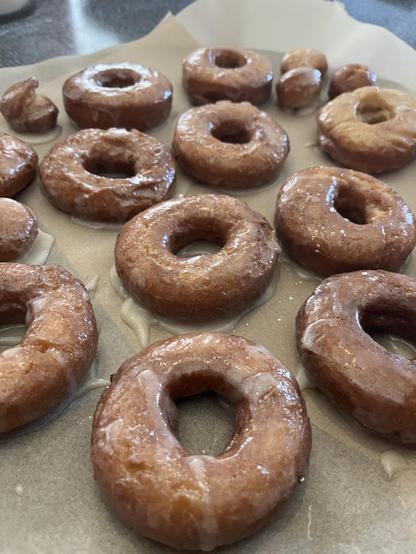 Up close photo of fresh glazed sour cream donuts on un bleached parchment paper on a bluish gray kitchen table.