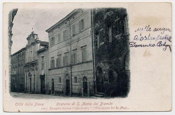 The image displays a vintage postcard with black and white imagery. The scene captures an architectural structure, presumably the Oratorio di S. Maria dei Bianchi in Città della Pieve as indicated by text on the card. It appears to be a historic building featuring classical European architecture, likely from the late 19th or early 20th century given its style and photographic quality.

The photo is monochromatic with varying shades of gray that suggest it may have been taken in black-and-white due to limitations at the time. There are handwritten inscriptions on the right side which seem to be names, possibly related to individuals who owned or created this postcard collection. The left edge shows a torn-off section indicating wear and age.

The bottom text provides context: "Città della Pieve" indicates the location of Città della Pieve in Tuscany, Italy; "Oratorio di S. Maria dei Bianchi" refers to an Oratory dedicated to Saint Mary of the White Friars (Bianchi). Further down it notes that Perugino painted the ceiling with a depiction of The Adoration of Magi.

The overall condition suggests this postcard has been preserved over time, showing signs of aging such as discoloration and some creasing. There is no direct indication of the specific historical period or context beyond these observations from the image itself.