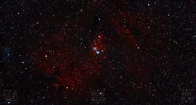 In a dark starfield with some hydrogen red on it, we can see a small cluster in the center. It's shaped rather like a Christmas tree that is mostly reddish.