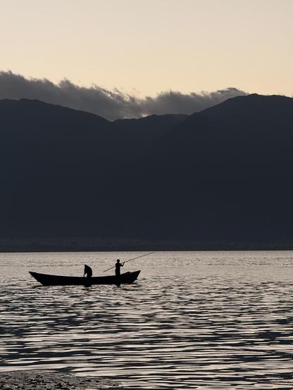 Silhouette of a boat with two people on lake Erhai in front of the mountains at sunset