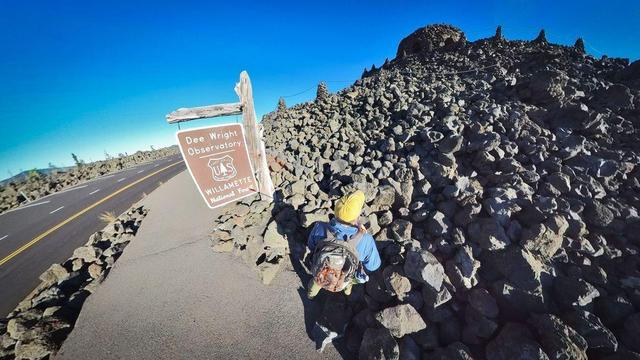 One of a series of photos showing a person hiking around a lava rock field in the Willamette National Forest of central Oregon, often observing distant mountains on the horizon, all under clear blue skies.