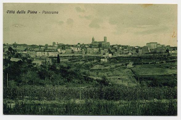 The image displays a vintage postcard showing Città della Pieve, an Italian town. The photograph captures the urban landscape of the town with buildings densely packed together in varying architectural styles and sizes. Prominent among these is a larger structure that appears to be a church or cathedral featuring towers, likely indicating its significance within the community.

The foreground shows agricultural fields, possibly fallow land, contrasting sharply with the developed area above it. The photograph has been rendered monochromatically, suggesting age, as this technique was common in early photography for postcards before color printing became widespread. Text on the image identifies the town and describes a panoramic view of Città della Pieve.

The overall quality is grainy, indicating an older print with some discoloration or wear over time. The photograph captures both urban life and rural elements together within one frame, offering a glimpse into the socio-economic landscape and architectural heritage of the region during its era of creation.
