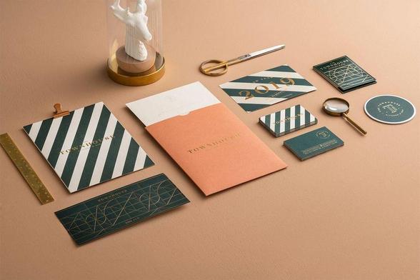 A stylish stationery collection featuring striped notepads, business cards, and a magnifying glass on a textured beige surface.