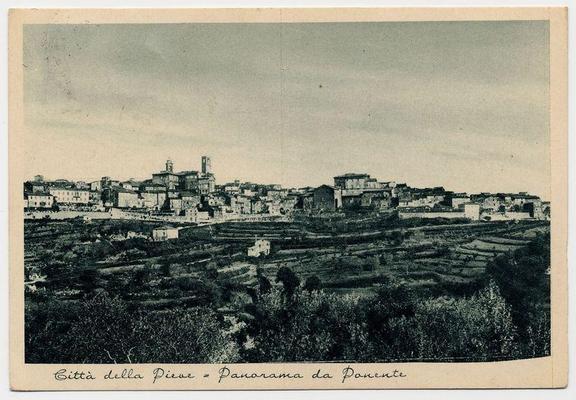 This image is a black and white photograph depicting an aerial view of Città della Pieve from the north. It shows a series of buildings clustered together, with what appears to be central structures such as towers or churches standing out due to their height above the surrounding architecture. The town's rooftops are spread across gently sloping hillsides, surrounded by patches that suggest agricultural fields and possibly vineyards. There is no visible modern infrastructure like roads or cars in this view.

A handwritten caption at the bottom of the image reads "Città della Pieve = Panorama da Ponente" which translates to English as "City of the Vow = Aerial View from West." The photograph has a vintage look, suggesting it was taken several decades ago. It appears aged with some discoloration and signs of wear on its edges.

The image captures the historical charm and layout of Città della Pieve in Italy's Tuscany region, emphasizing its traditional architecture set against a rural backdrop.