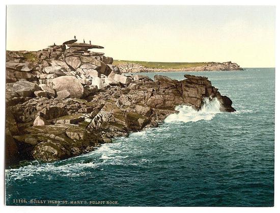 The image depicts a rugged coastal landscape, likely taken during the late 19th century judging by its style. The scene shows an extensive rocky outcrop jutting into the sea on what appears to be St Mary's in the Scilly Isles of Cornwall, England.

On top of the highest rock formation, there are several individuals who seem to be exploring or possibly fishing, standing with a sense of precariousness over the edge where waves crash against the rocks. The water is a deep blue-green color and churns energetically as it strikes the jagged outcrops.

The land in the background appears flat and covered with grasses and shrubs indicative of coastal vegetation that withstand salty conditions, stretching into what looks like a horizon line suggesting an open expanse beyond. This could be part of another island or simply distant coastline seen from this rocky formation's perspective.

There is no visible sky as it seems to blend seamlessly with the water at the horizon due possibly to atmospheric lighting effects common in such prints during that era, which often used photographic techniques like colorization to enhance certain features for artistic effect. The image carries a sense of isolation and natural beauty typical of remote British Isles coastal scenes.

The photo is marked '1064: SCILLY ISLES ST MARY'S PULPIT ROCK' along with an identification number, which suggests it's p [...]