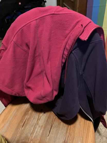 Two jackets, one in a bright pink, one in a darker violet are hanging on a chair.