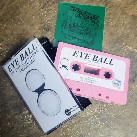 A photo of the new Eye Ball cassette (it's pink) and its case, and a sticker from Knuckles on Stun, the tape distributor