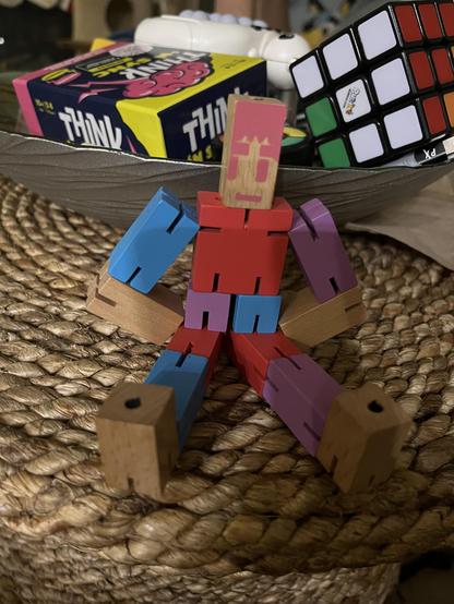 A wooden figure made from articulated blocks. Sitting with its legs spread wide.