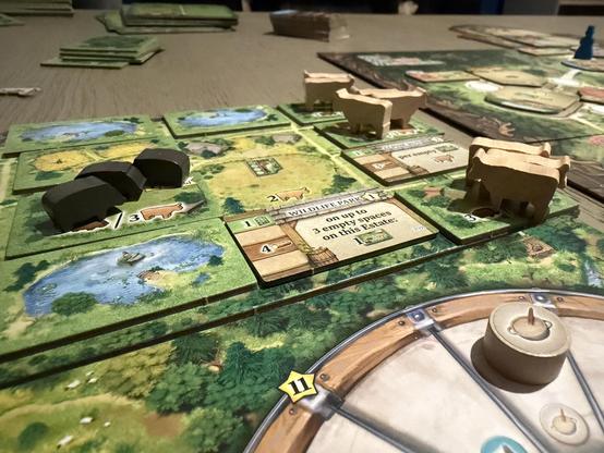Shot of a Black Forest play board. Three pigs on the board. Nine cows. Various cardboard building tiles. The production wheel is just in shot. What’s that? Yeah it’s the porridge marker just visible.