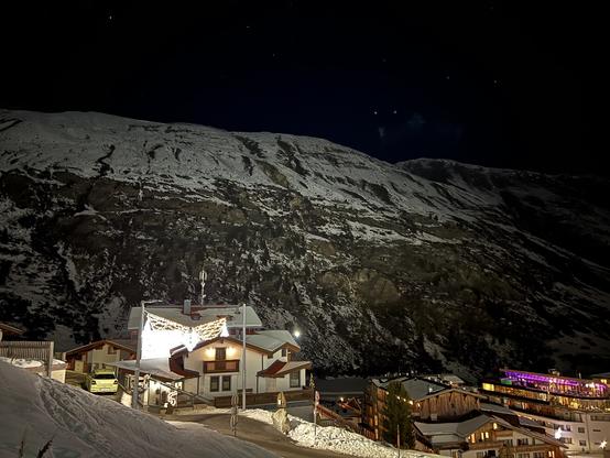A snowy mountain over a village, in the dark. The houses are lit up.